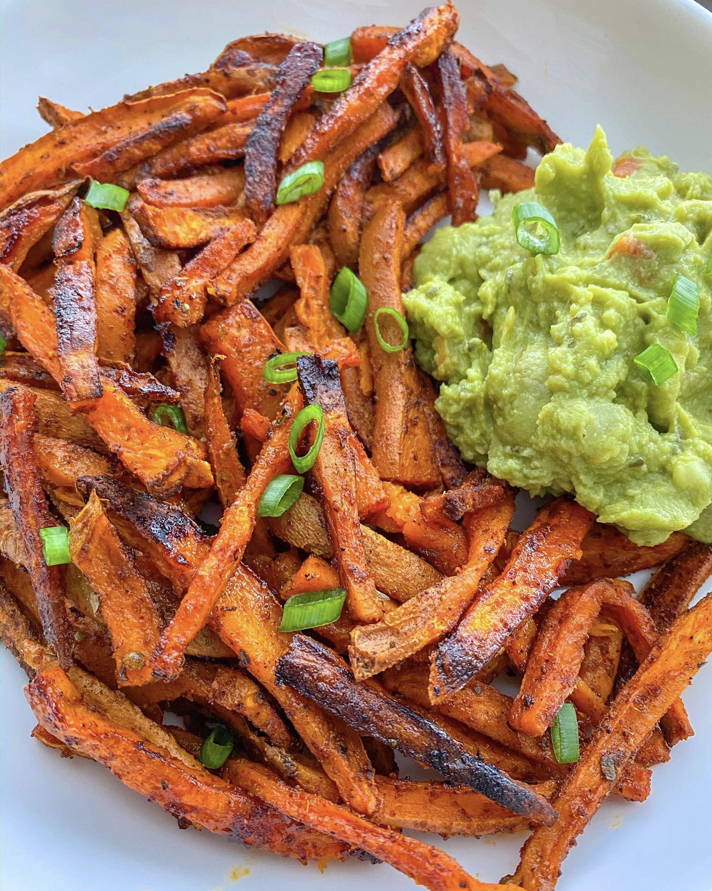 Sweet potato fries on a white plate with a side of guacamole. 