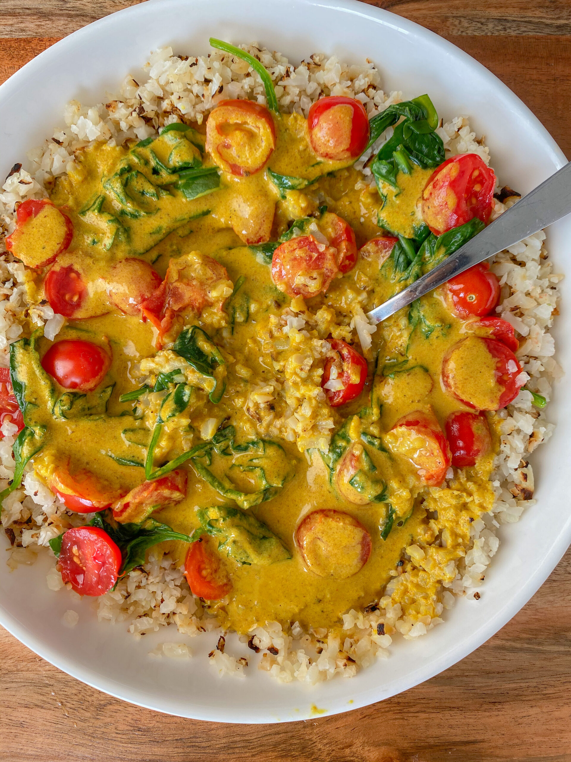 Overhead shot of coconut curry in a white bowl with a silver spoon. 