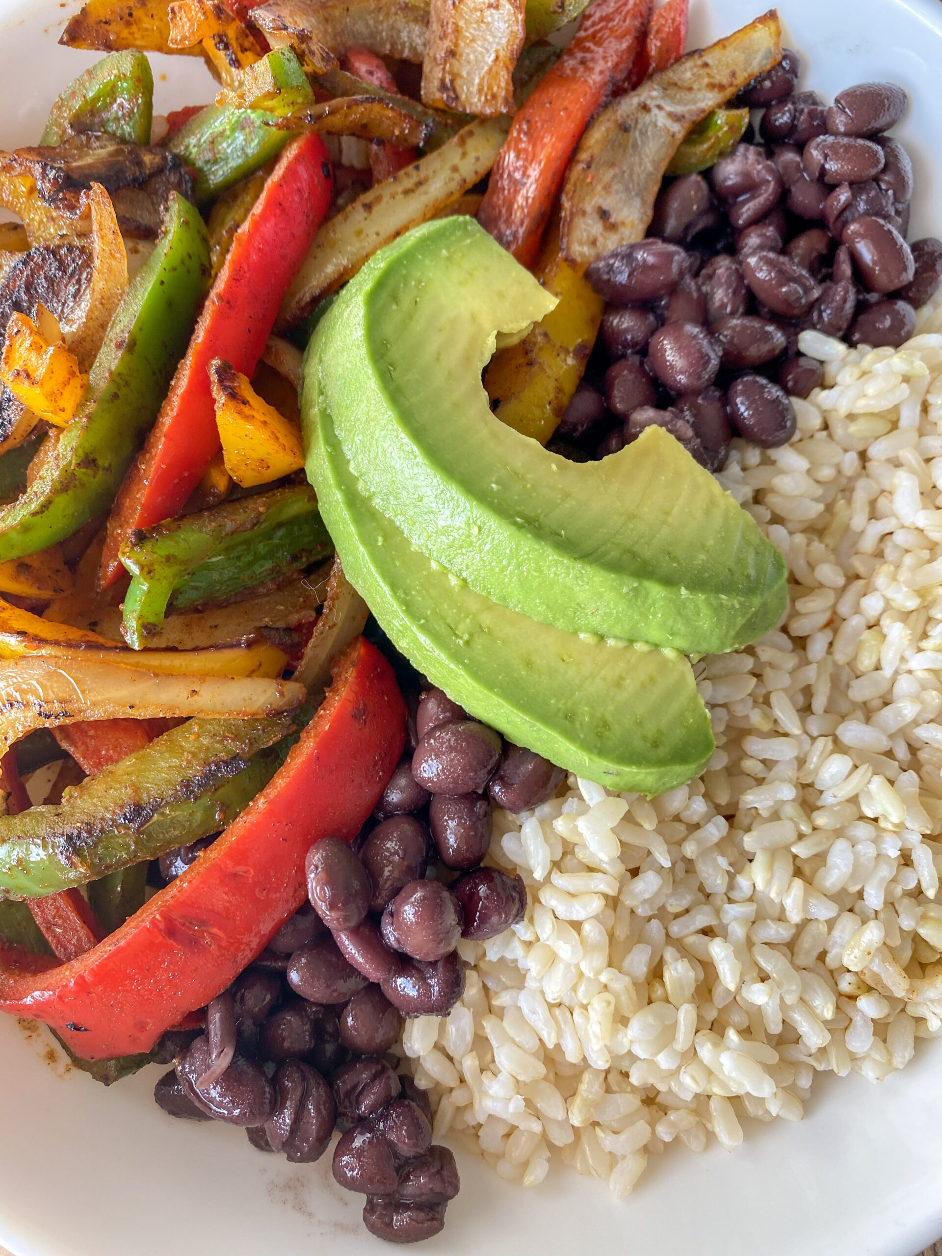 Veggie Fajitas served over rice and beans with sliced avocado.