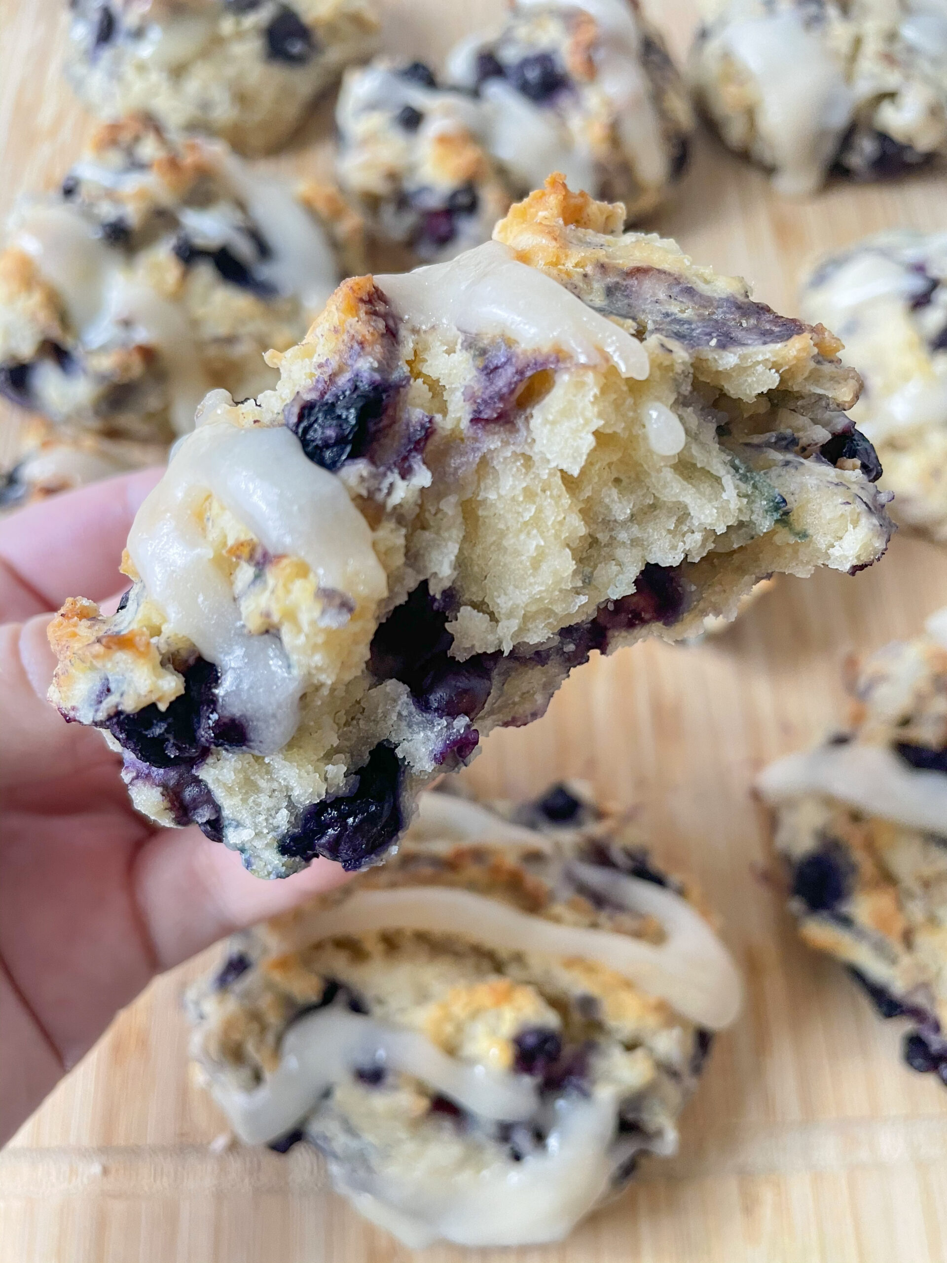 Hand holding a vegan blueberry drop biscuit with a bite taken out of it and more biscuits in the background. 