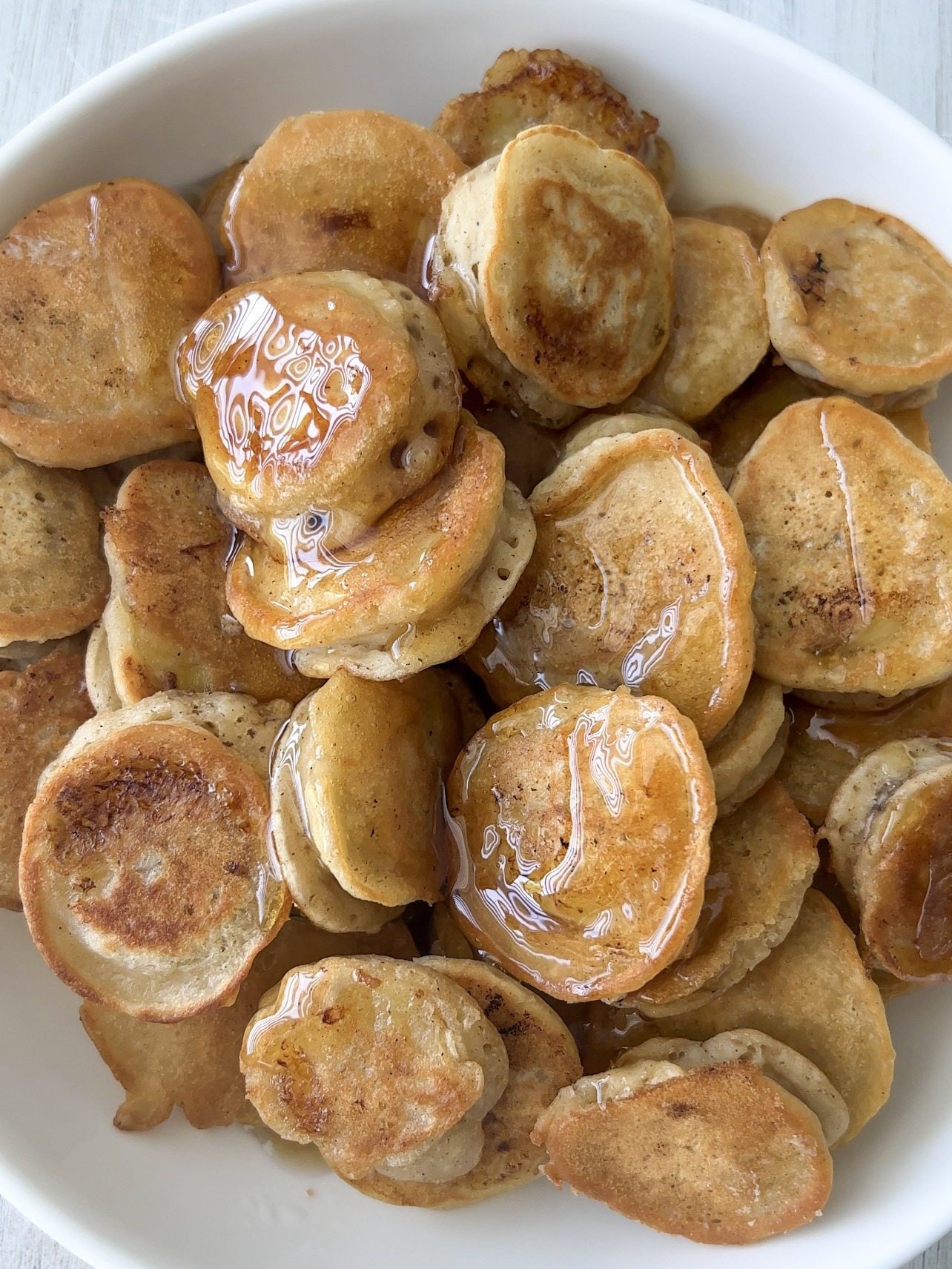 Mini banana pancake bites on a white plate with maple syrup on top. 