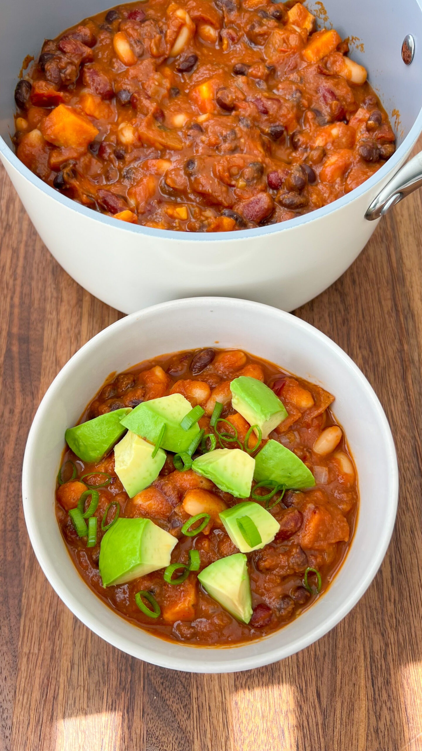 Large pot of pumpkin chili next to a white bowl of chili topped with avocado. 