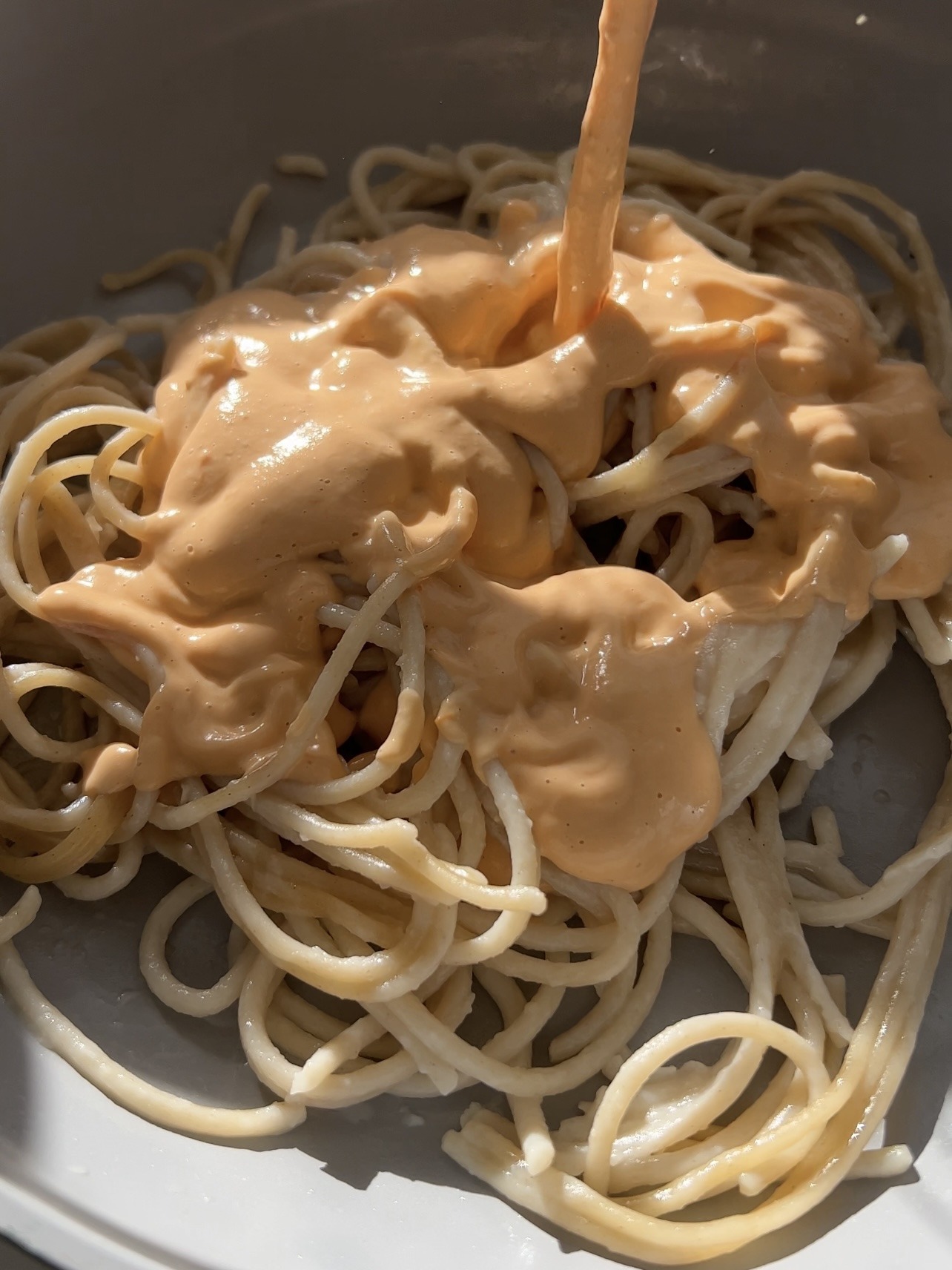 Noodles in a bowl while roasted tomato sauce is being poured on top. 