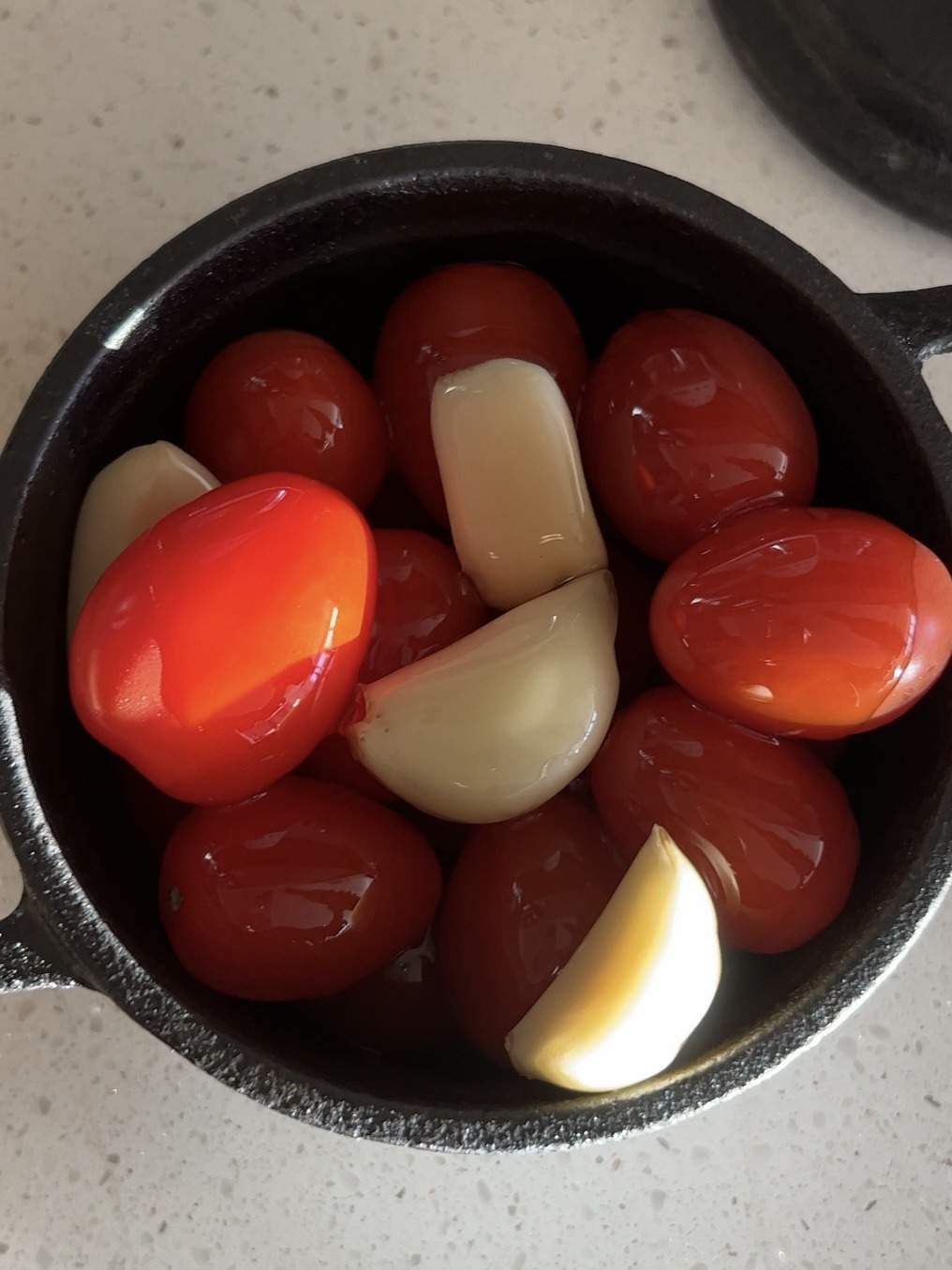 Tomatoes and garlic in a cocotte drenched in olive oil. 