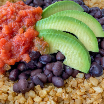 Cauliflower burrito bowl topped with black beans, salsa and avocado slices.