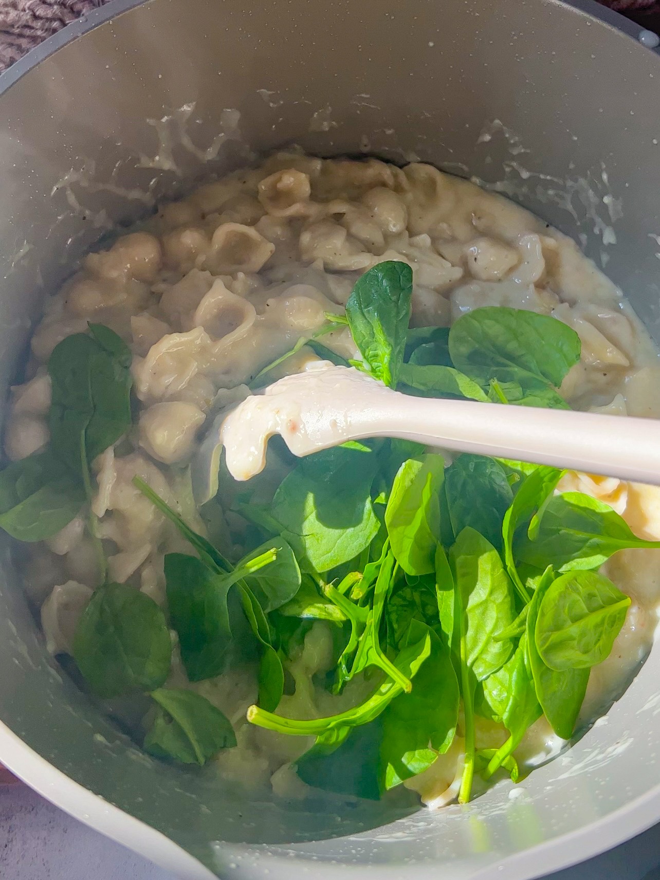 adding the noodles and spinach to the creamy garlic pasta sauce