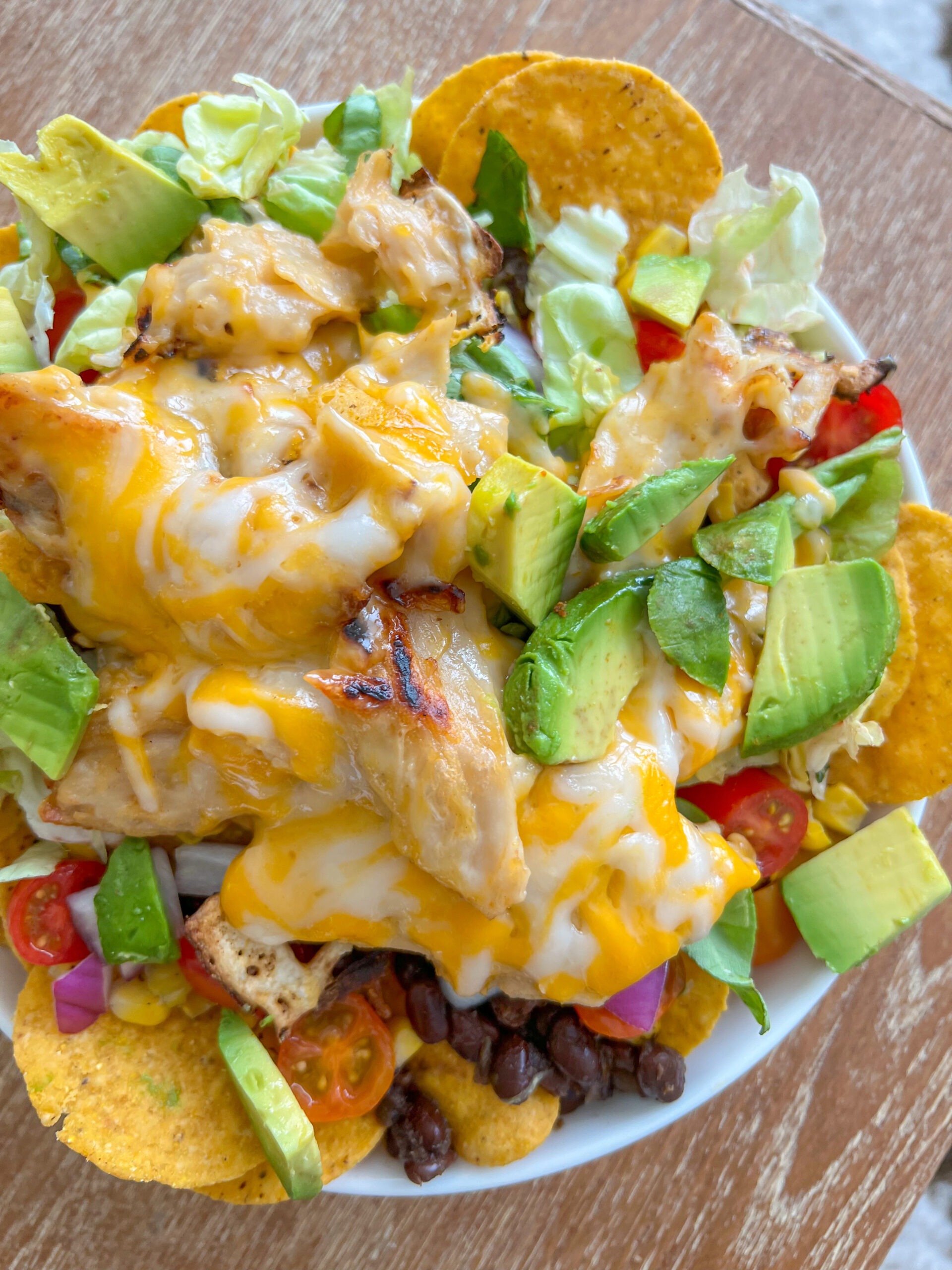 vegan chicken nachos topped with avocado, black beans, cheesy chicken, tomatoes, onion, etc