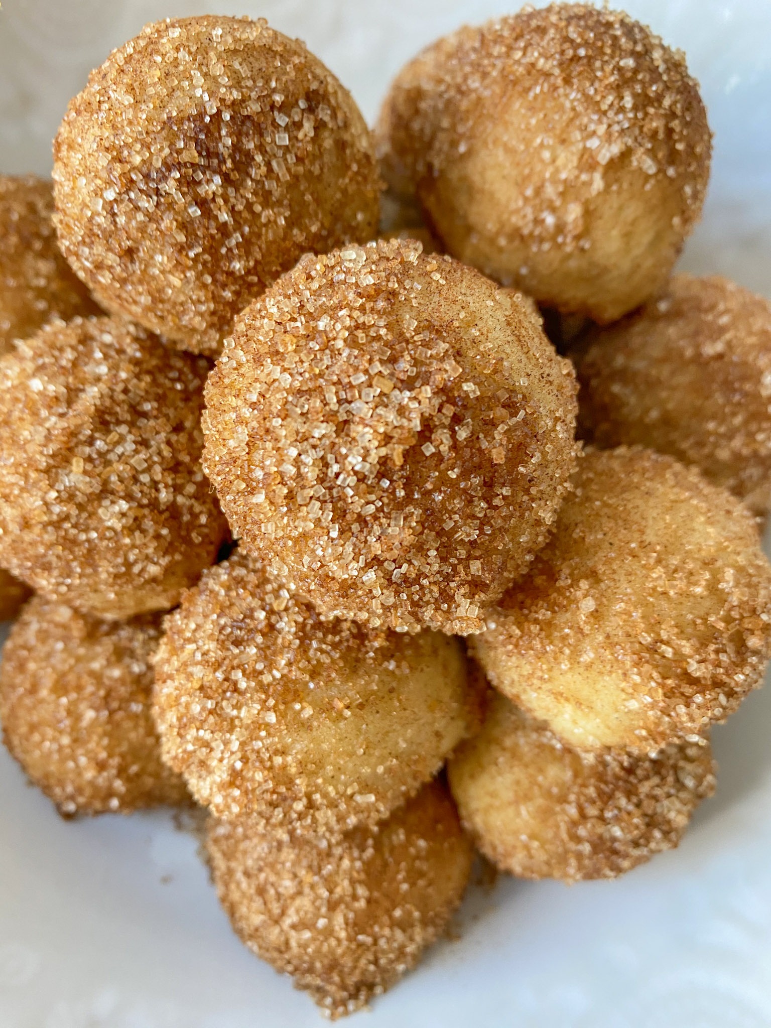 close up shot of cinnamon sugar donut holes stacked on a white plate. 