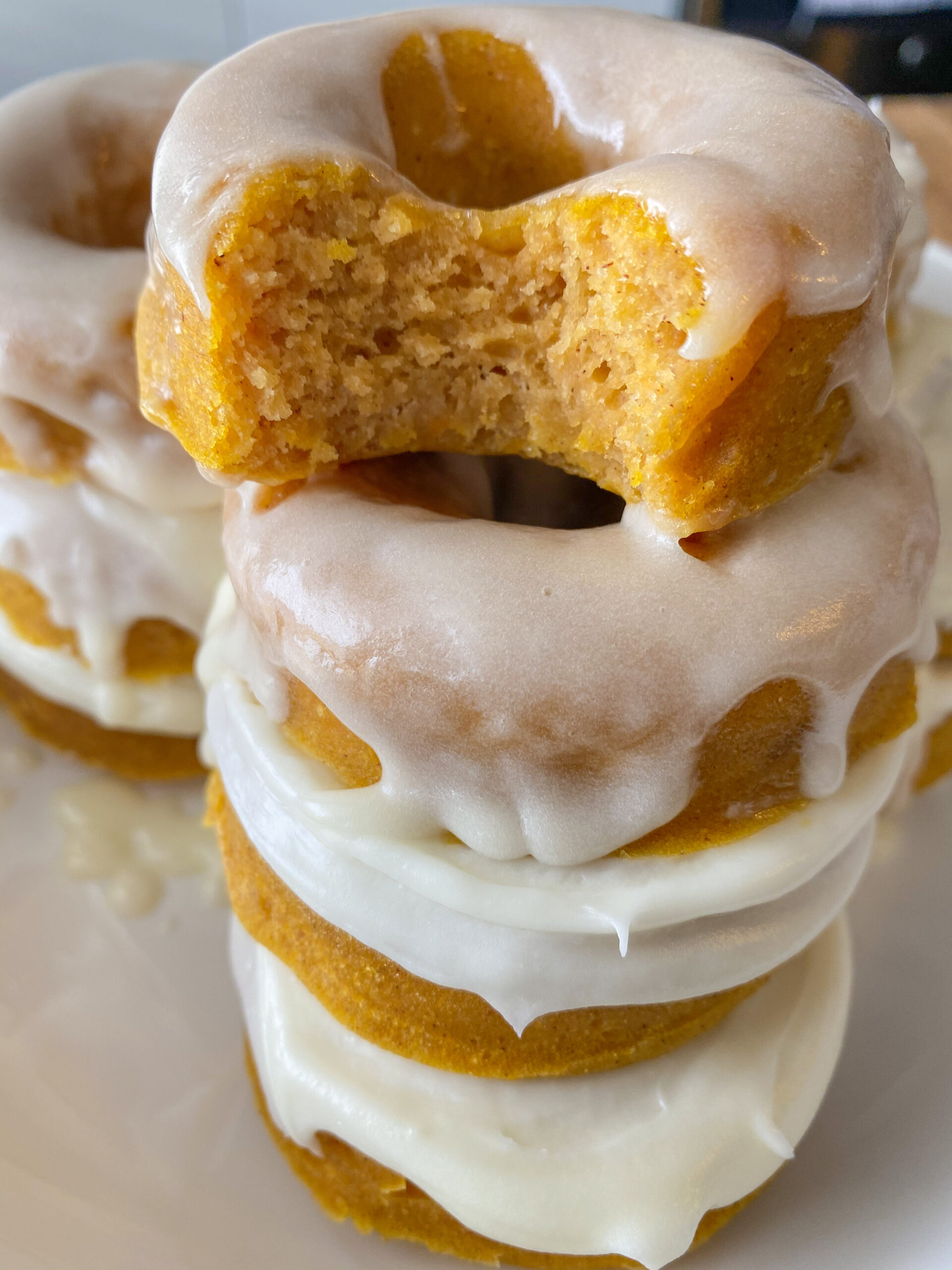 Pumpkin donuts stacked on top of each other with the top donut with a bite taken out of it. 