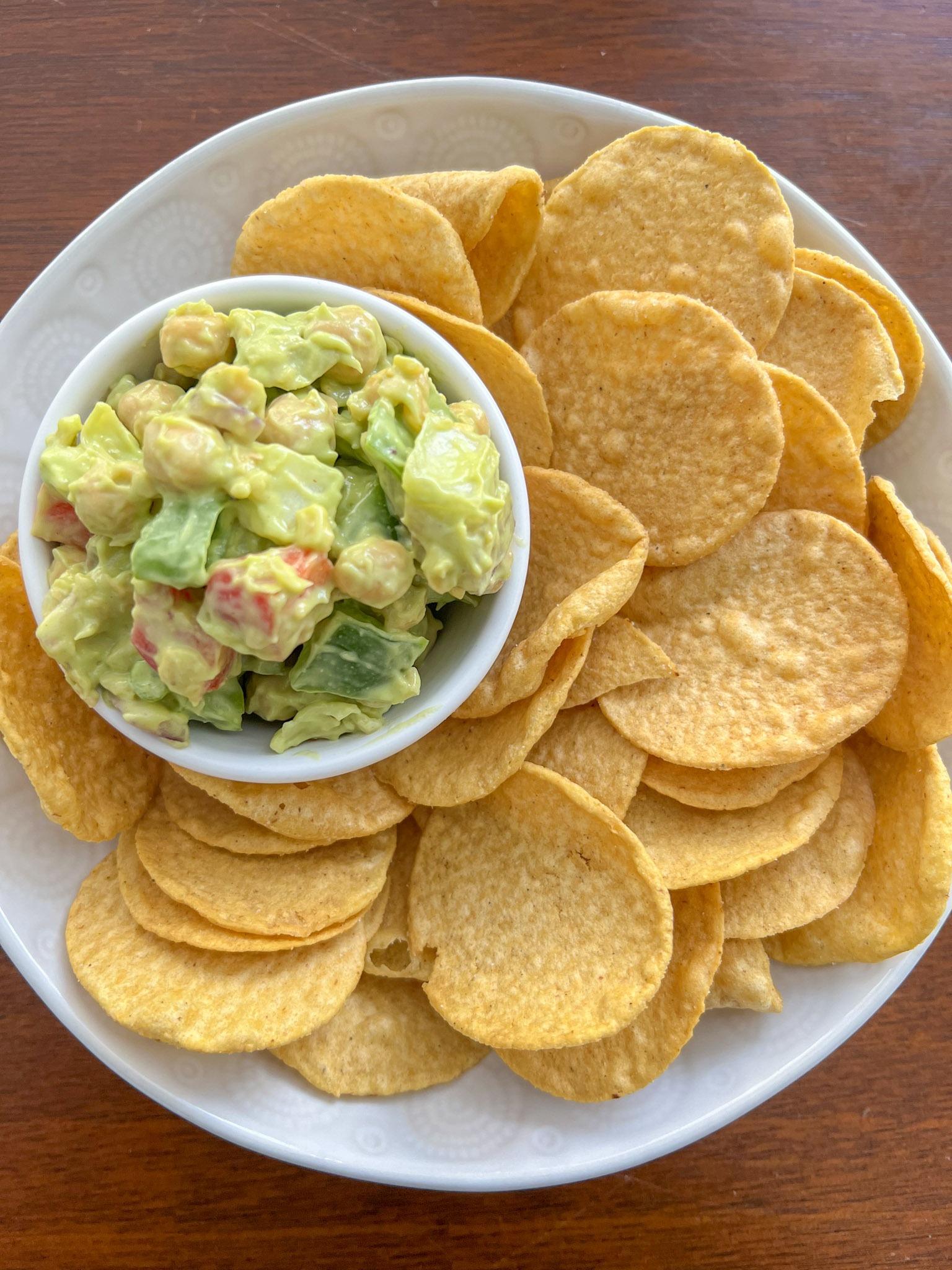 Avocado and chickpea salad in a small bowl with tortilla chips on a white plate. 