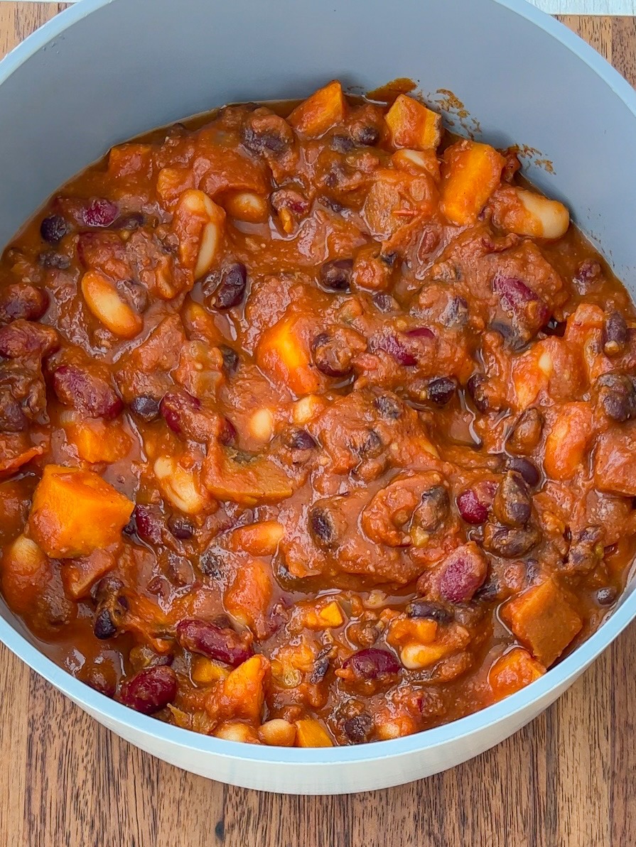 Top view of vegan pumpkin chili in a grey pot with a wooden background. 