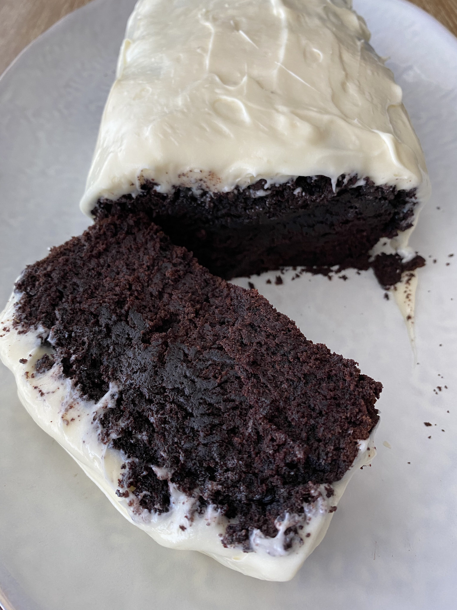 Chocolate vegan cake with frosting on a white plate with one piece sliced off. 