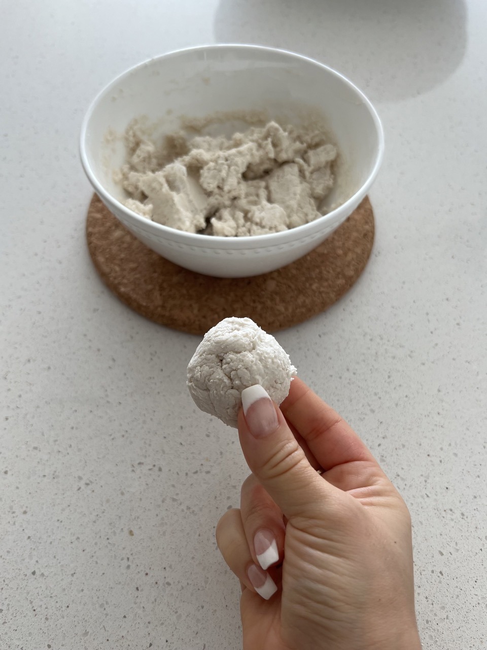 Bagel dough in a white mixing bowl with a hand holding one ball of dough. 