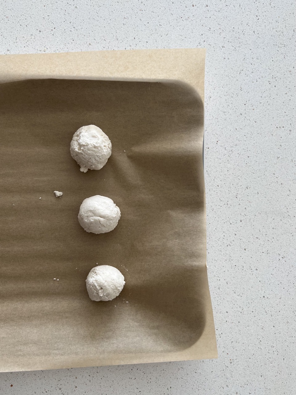 Raw bagel bites lined up on a parchment lined baking sheet. 