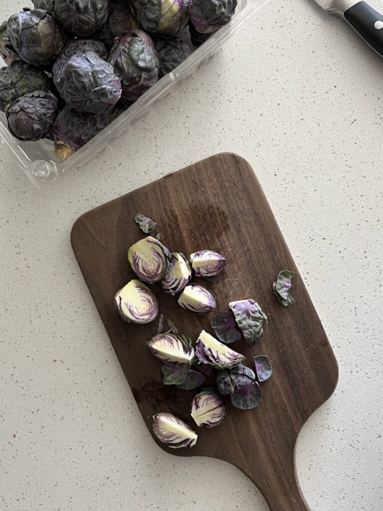 Brussels sprouts being chopped on a wooden cutting board. 