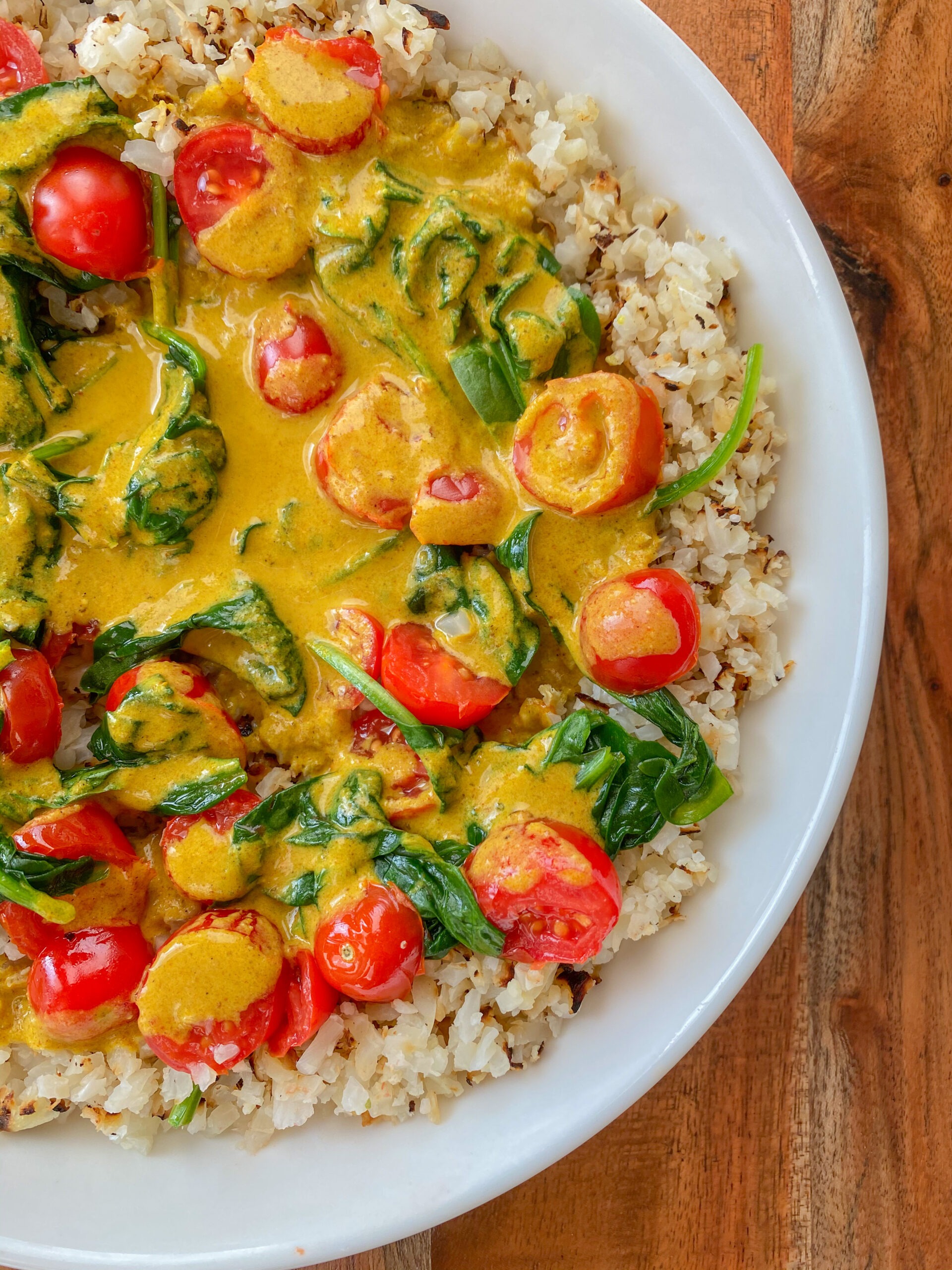 White bowl with cauliflower rice topped with curry and tomatoes and spinach. 