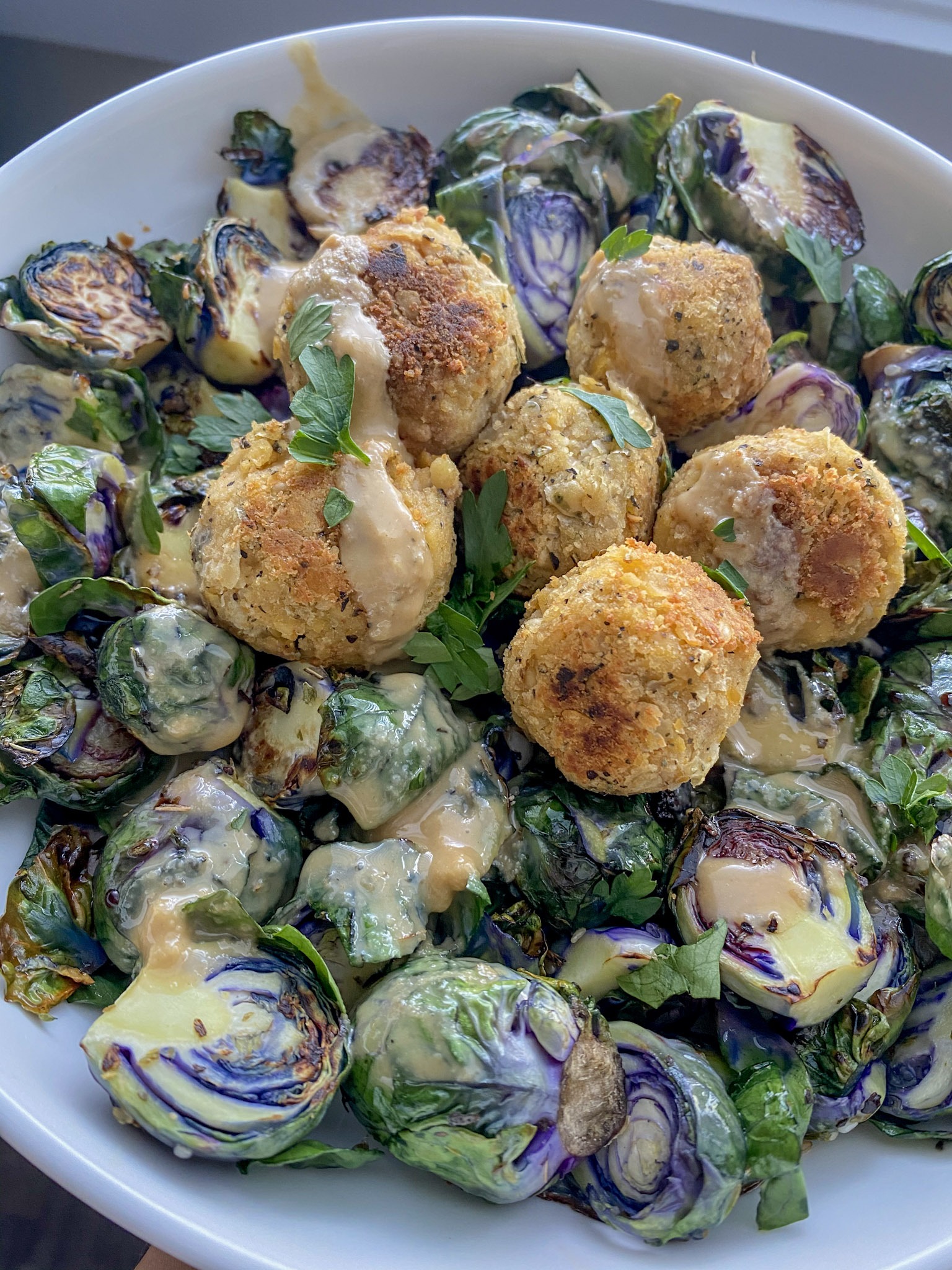 Brussels sprouts in a white, shallow bowl with chickpea meatballs on top. 