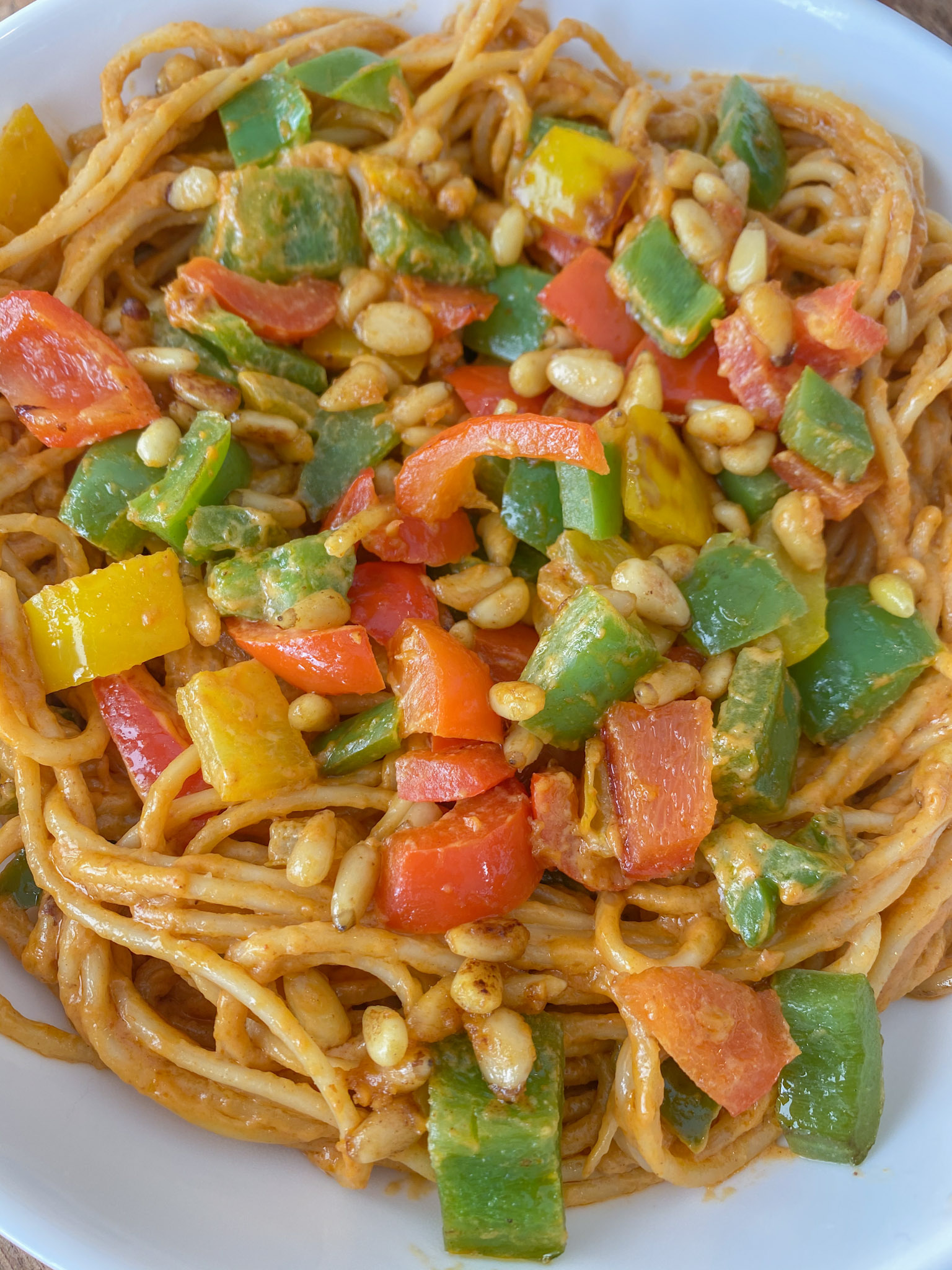 Vegan peanut noodles topped with bell peppers in a white bowl. 