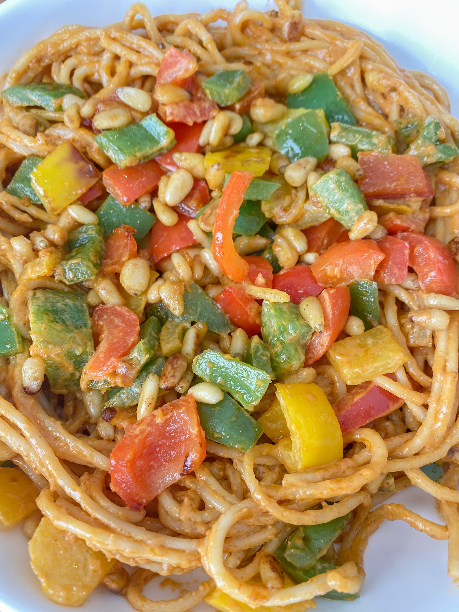 Close up shot of peanut sauce noodles topped with veggies in a white bowl. 