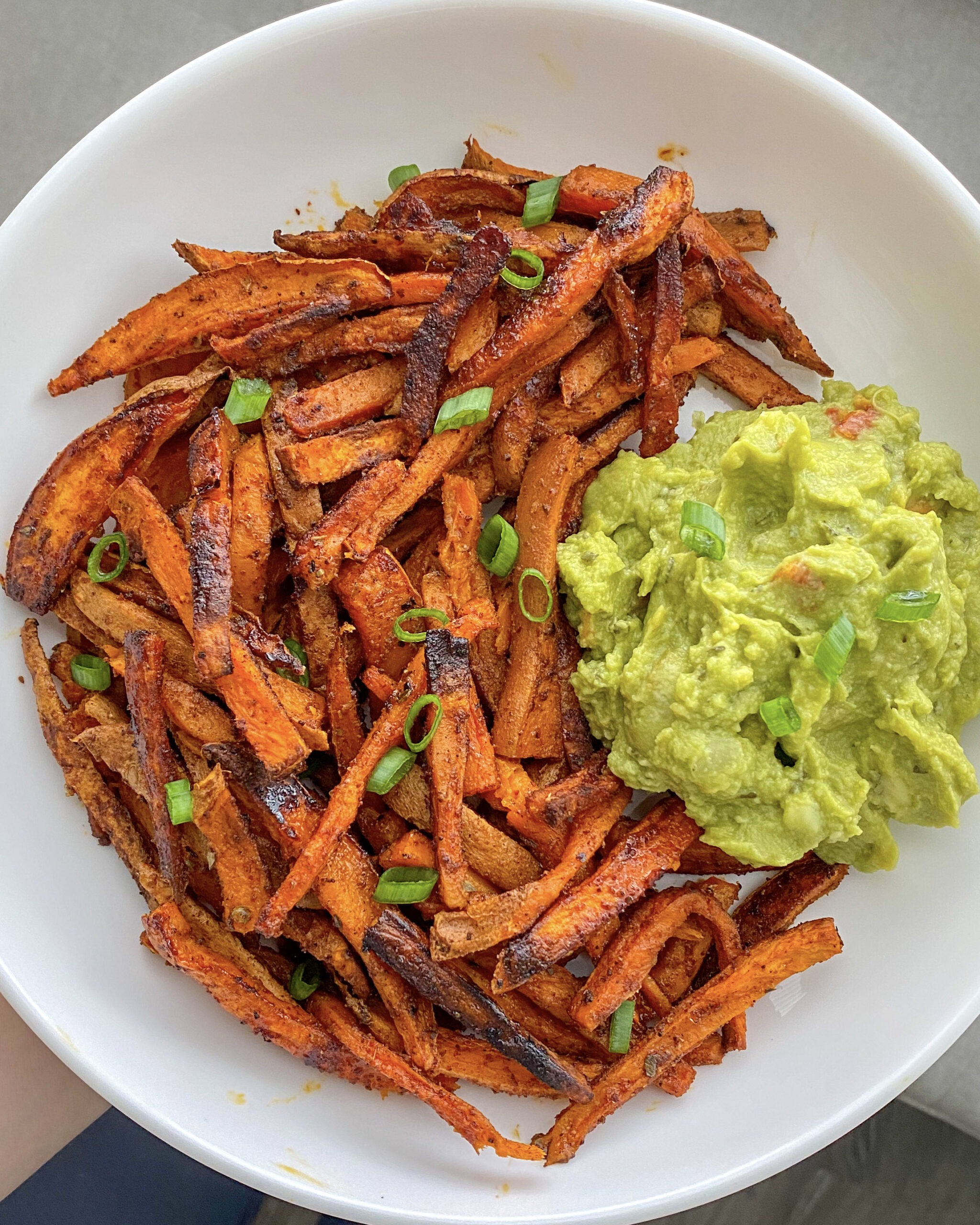 Sweet potato fries in a white bowl with guacamole. 