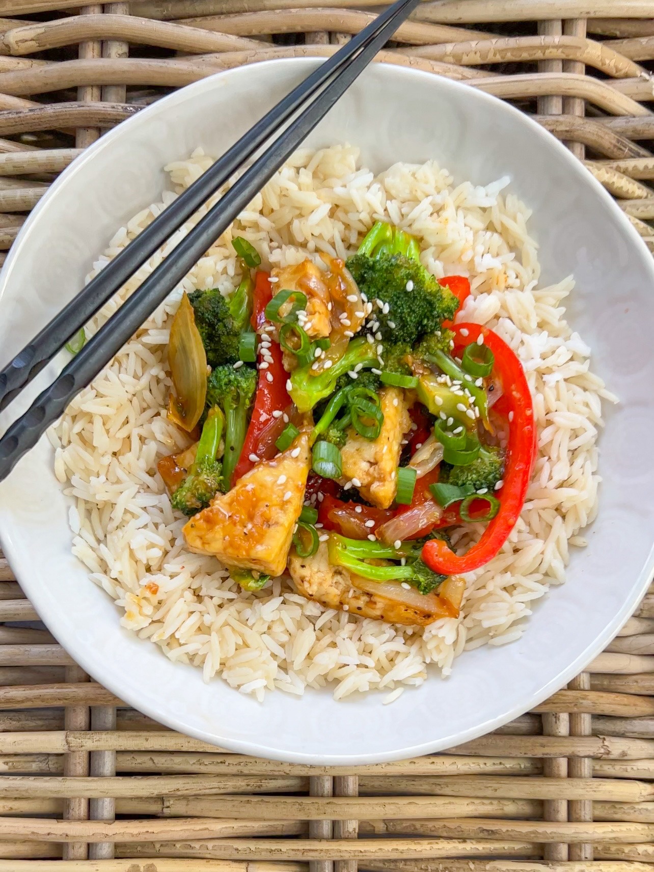 Tofu stir fry served over rice in a white bowl.