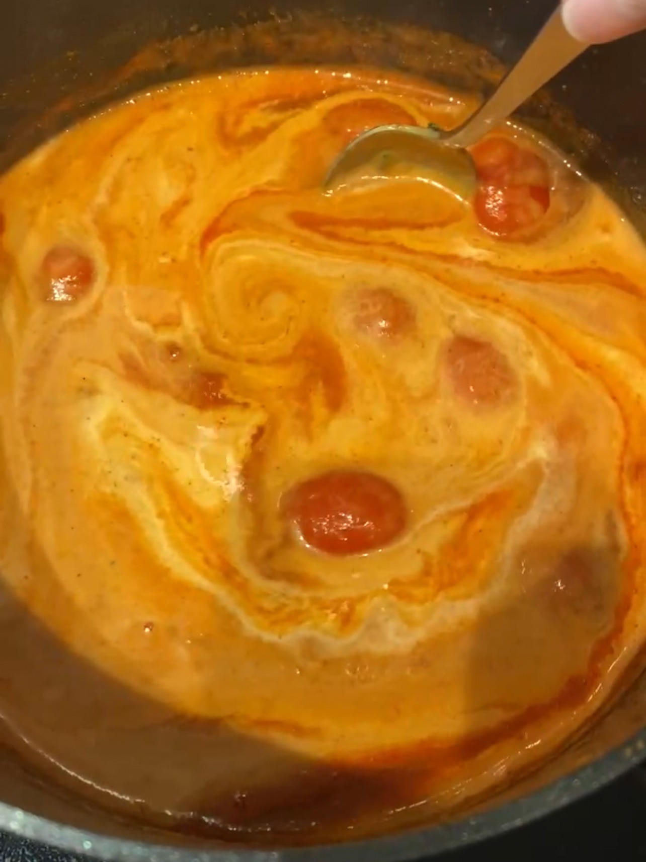 Adding coconut milk to tomato sauce.