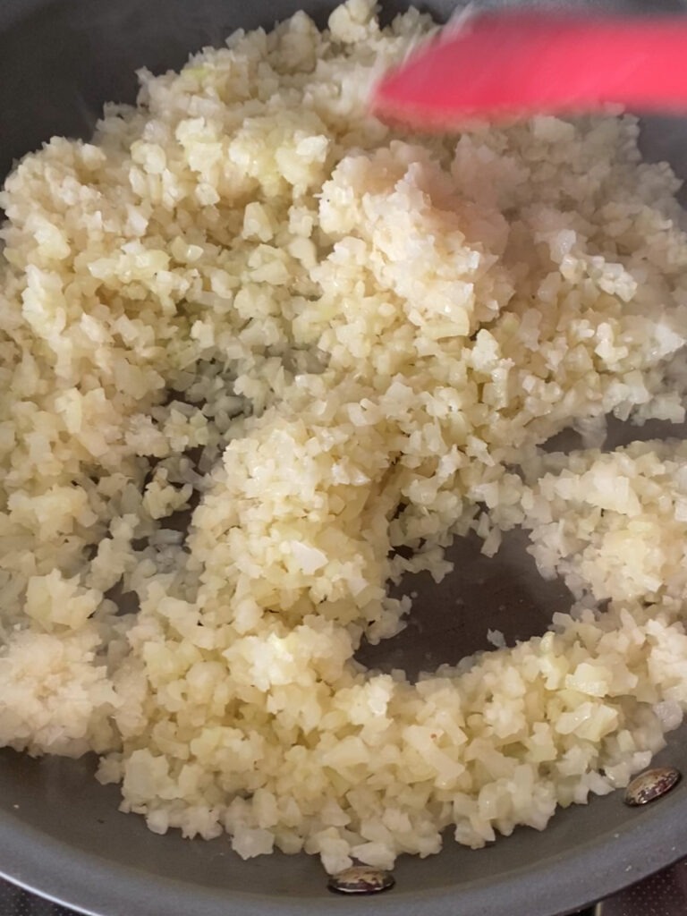 Cauliflower rice starting to cook in a sauté pan. 