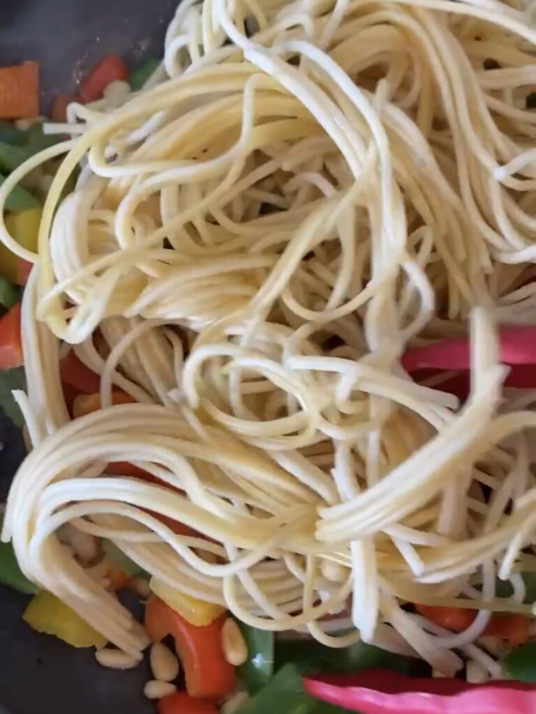 Cooked noodles being added to the peppers and peanuts.