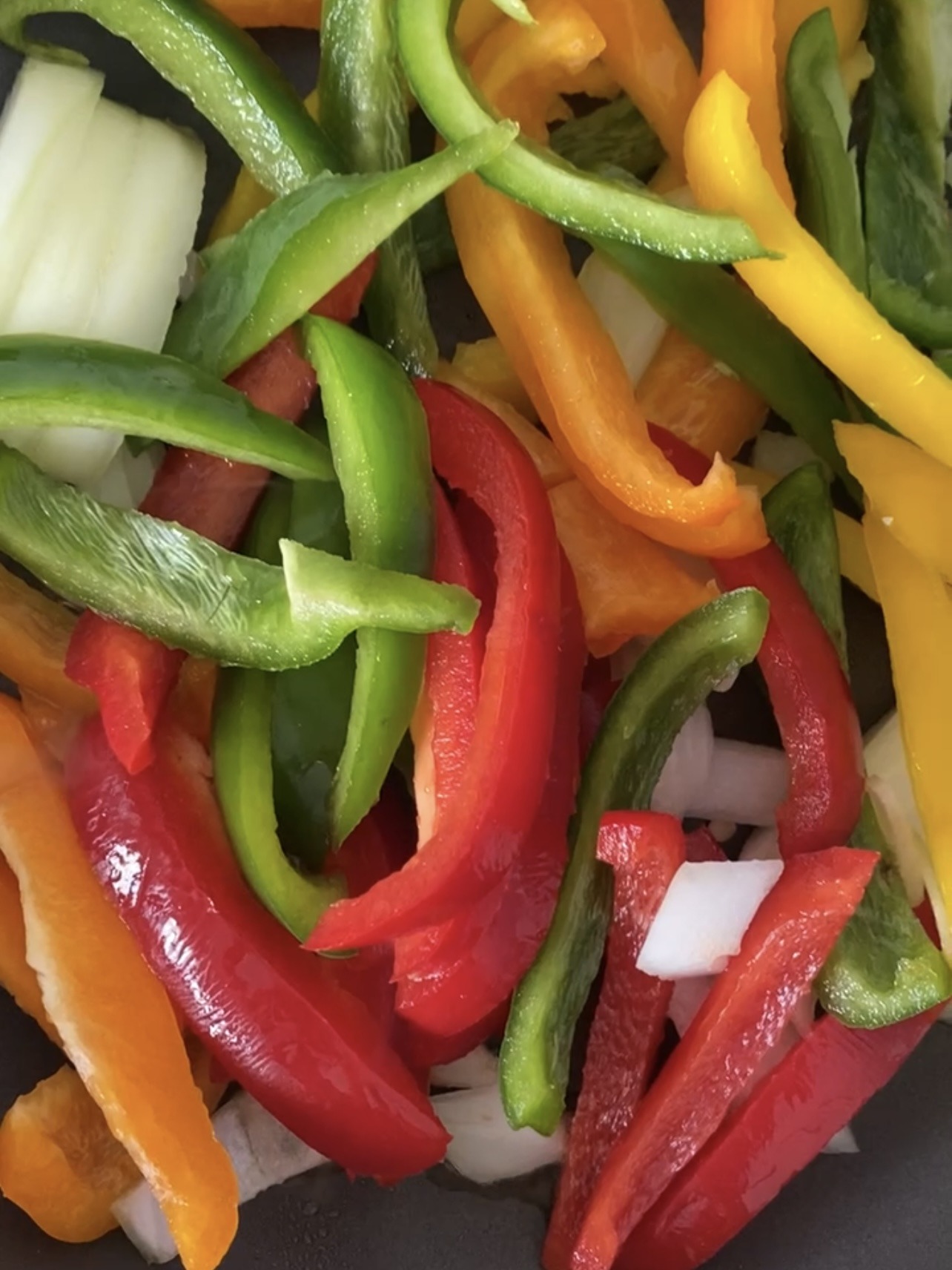 Adding sliced peppers and onions to a hot skillet.