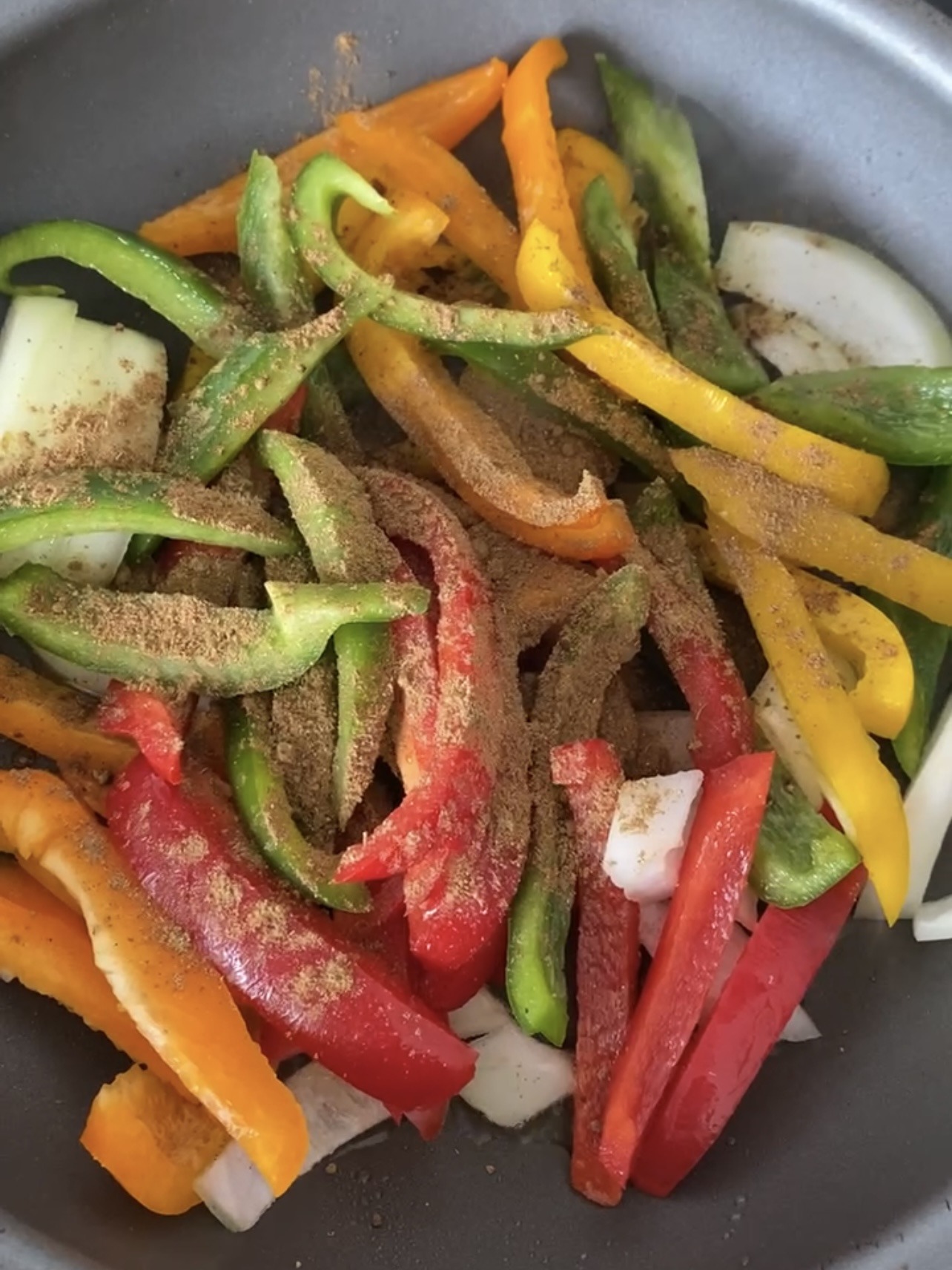 Adding seasoning to peppers and onions in a pan.