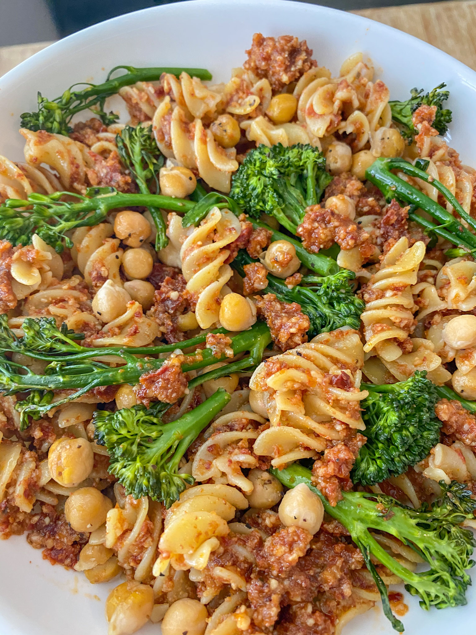 Vegan Sun-dried Tomato Pesto Pasta served with broccoli in a white bowl.