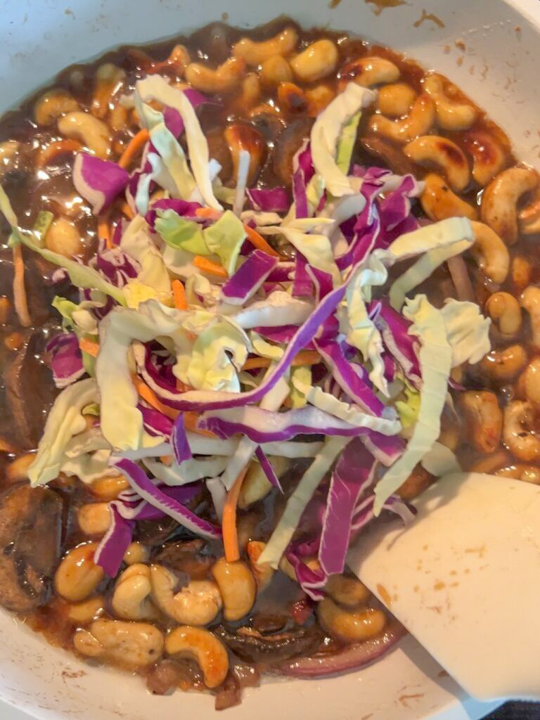 Cashews, teriyaki sauce and shredded vegetables in a white sauté pan. 