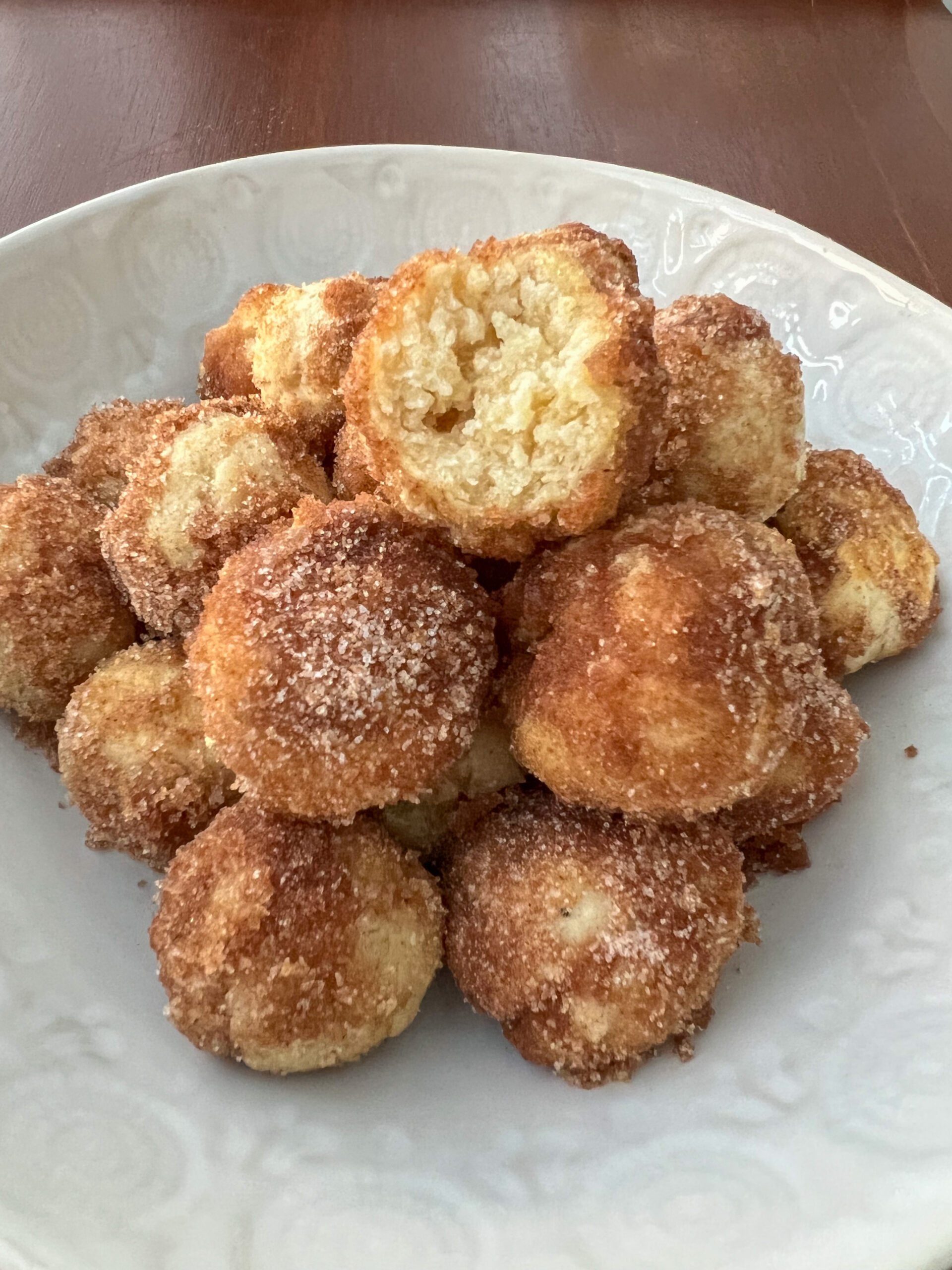 Cinnamon sugar bagel bites stacked on a plate with the top bagel missing a bite. 