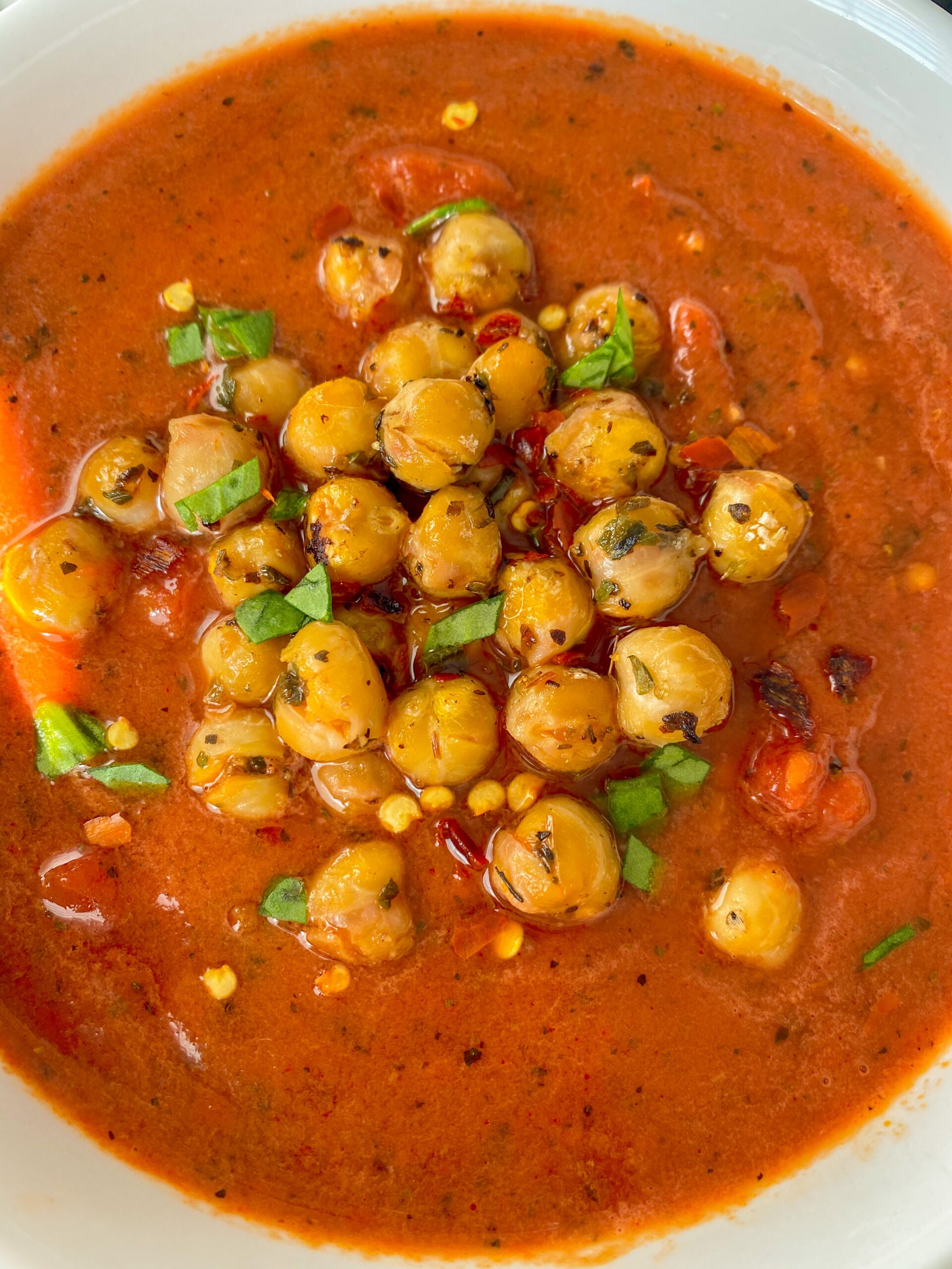 Tomato basil soup topped with chickpeas in a white bowl.