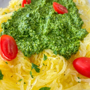 Spaghetti squash pasta topped with pesto sauce and cherry tomatoes.