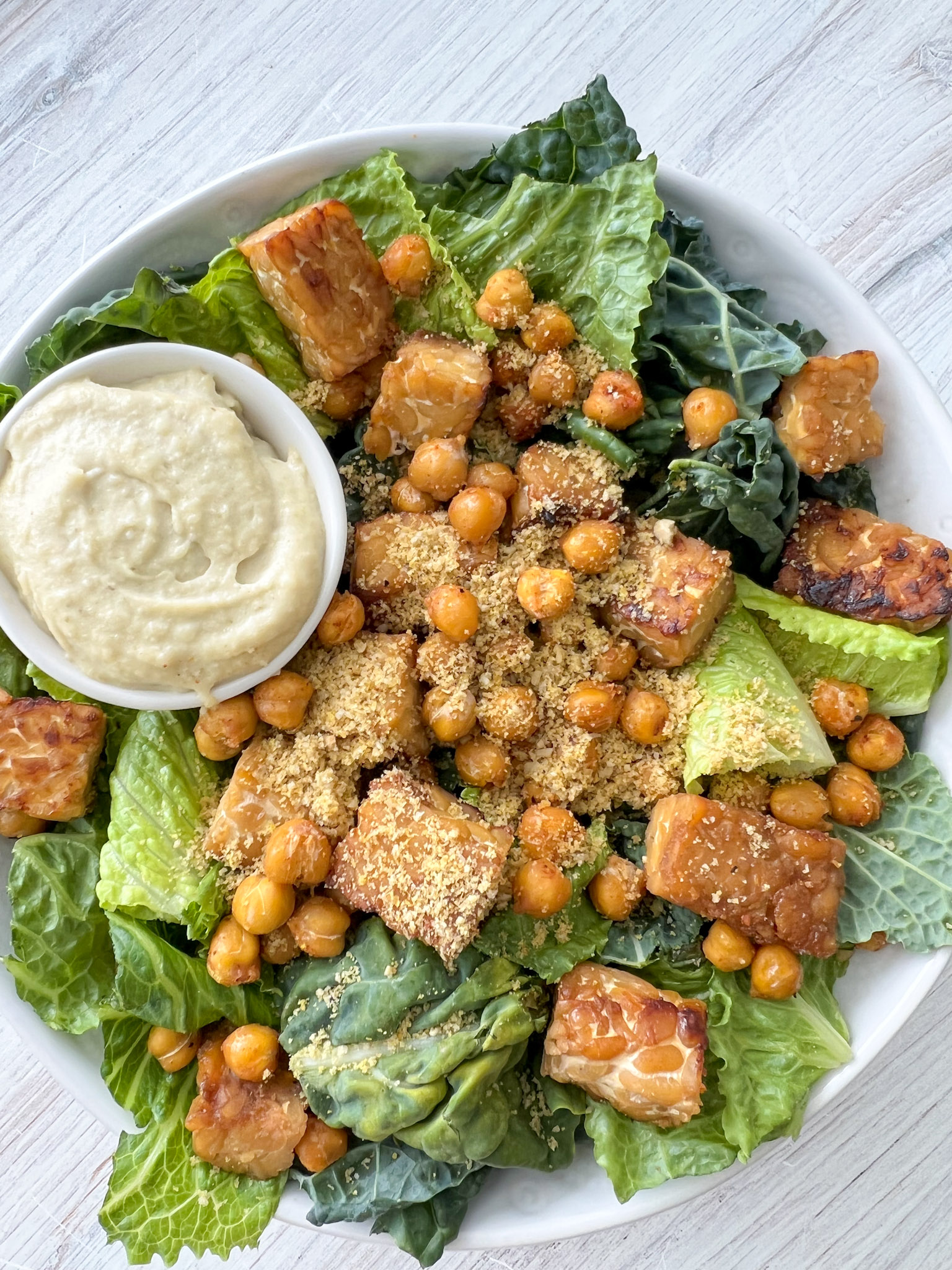 vegan caesar salad in a white bowl with dressing on the side. 