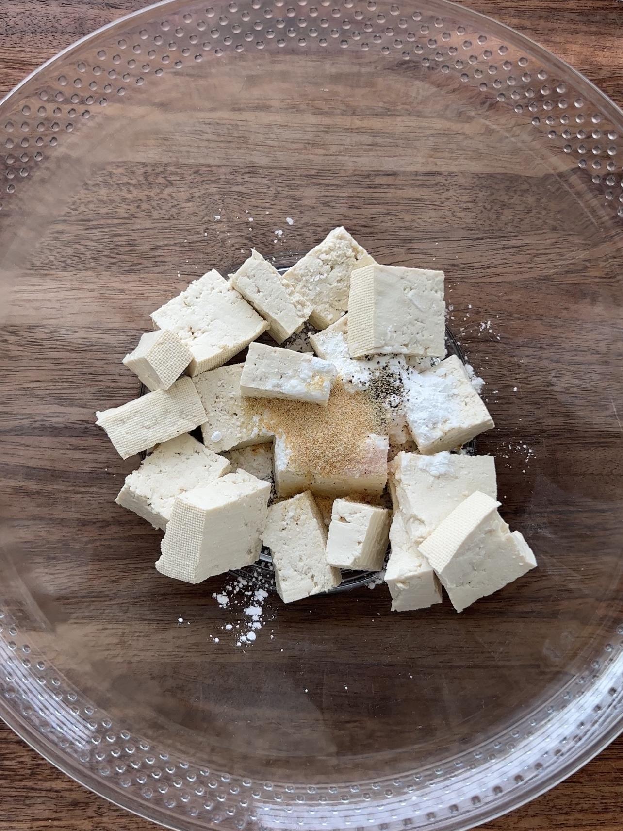 seasoning the tofu in a bowl with cornstarch, garlic powder, salt, and pepper