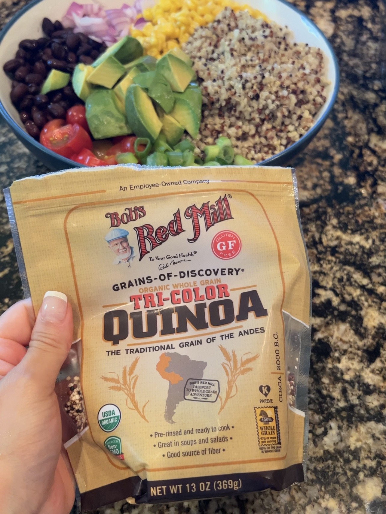 Hand holding a back of quinoa with the black bean quinoa salad in the background. 