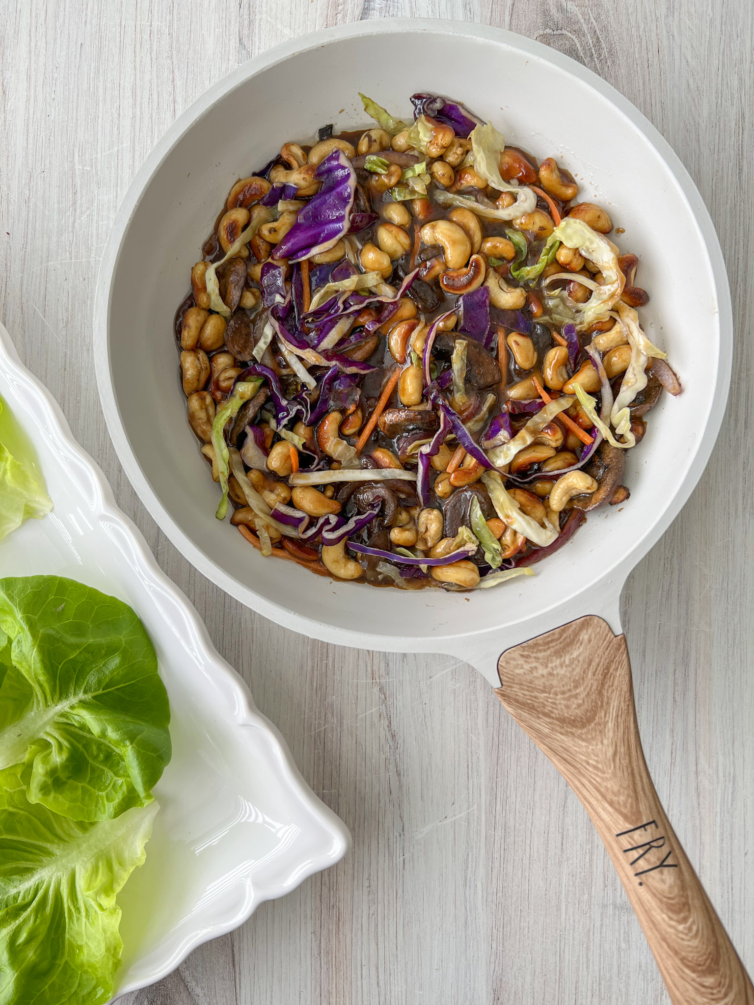 Cashew teriyaki mixture in a sauté pan next to a serving platter with lettuce on it. 